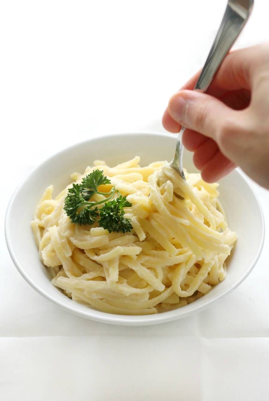 hand and fork with bowl of gluten-free fettuccine alfredo