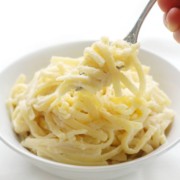 fork scooping vegan gluten-free fettuccine alfredo out of white bowl