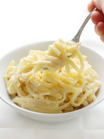 fork scooping vegan gluten-free fettuccine alfredo out of white bowl