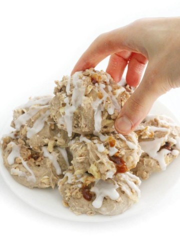 pile of stuffed caramel apple cookies on white plate with hand grabbing top
