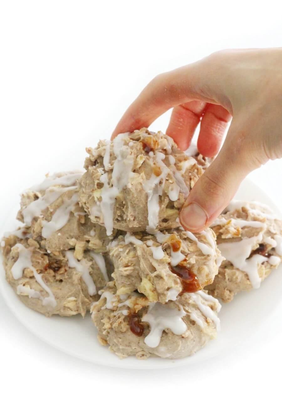 pile of stuffed caramel apple cookies on white plate with hand grabbing top
