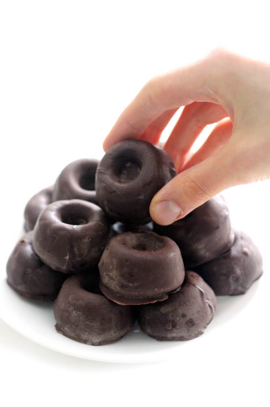 hand grabbing a gluten-free chocolate-covered mini doughnut from plate