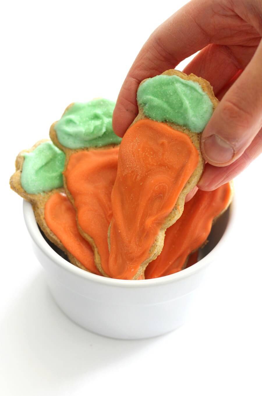 hand grabbing a decorated gluten-free carrot cake sugar cookie from white bowl