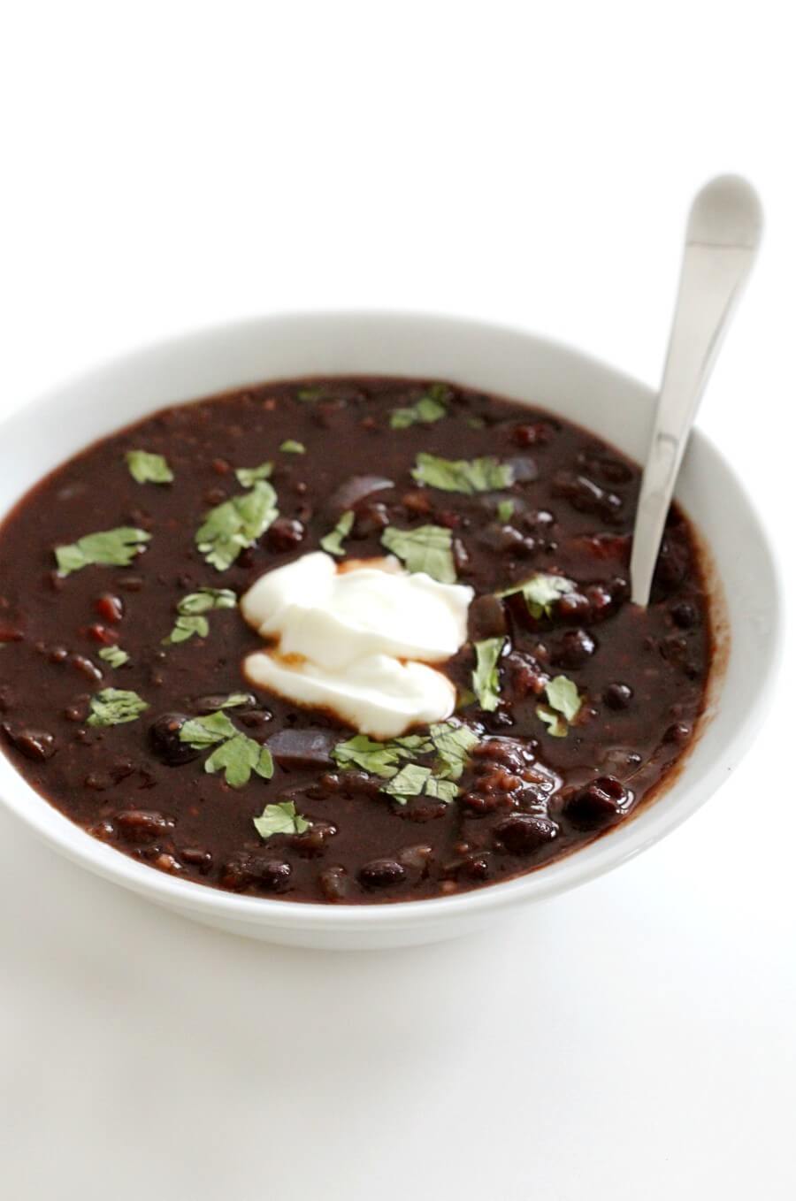 white bowl of spicy chipotle black bean soup with sour cream and spoon