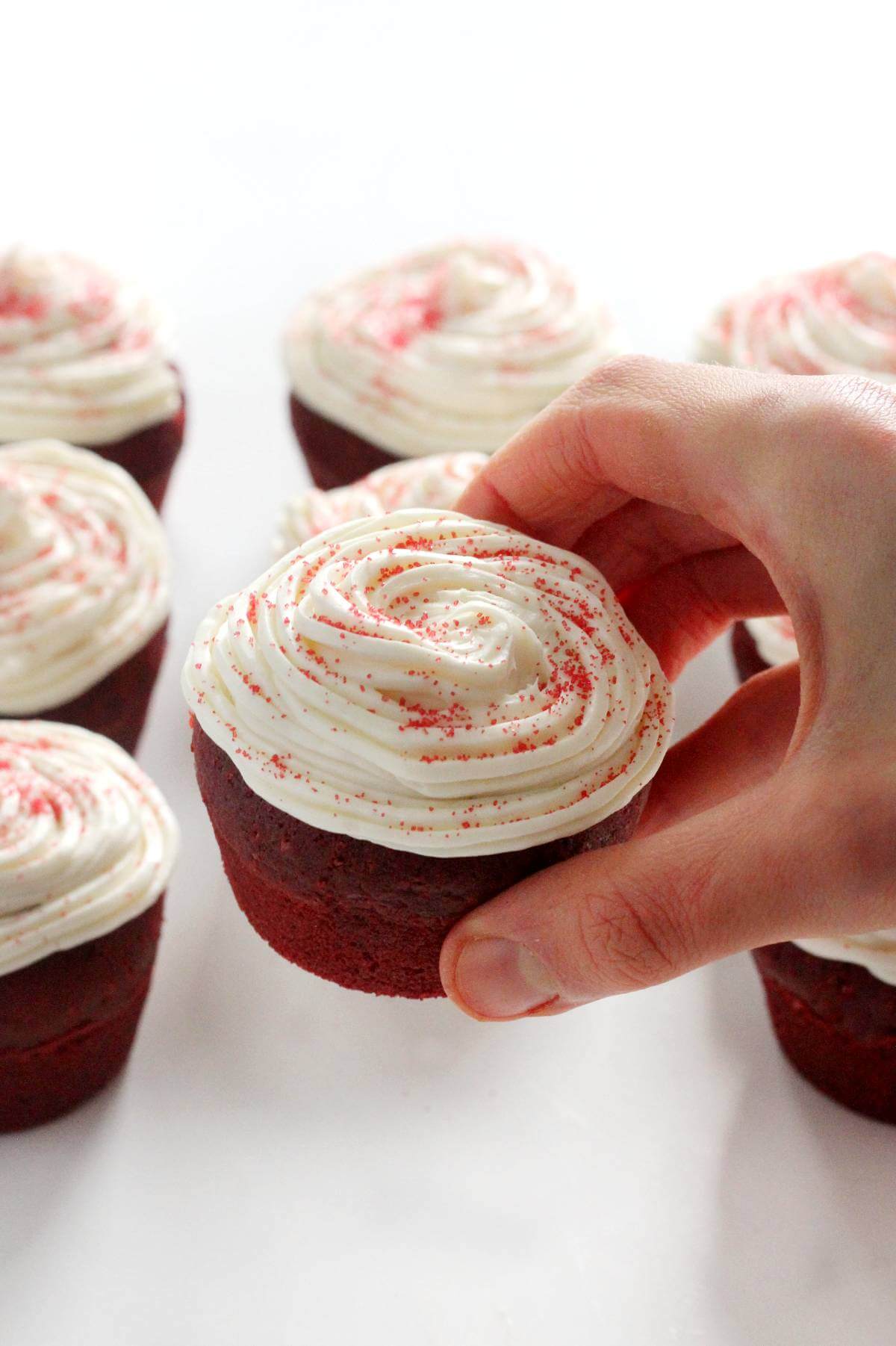 hand grabbing a frosted gluten-free red velvet cupcake