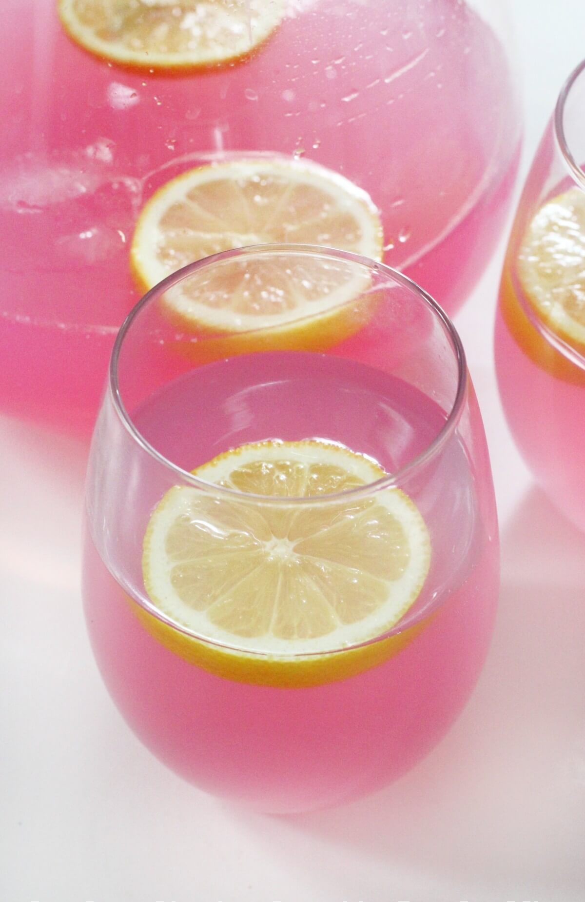 pitcher and close up of fresh glass of pink lemonade with lemon slice