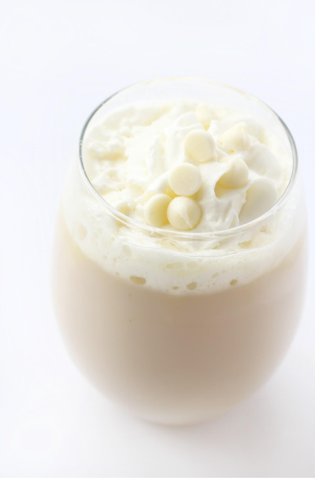 close up of vegan white hot chocolate in a glass with white chocolate chips and whipped cream