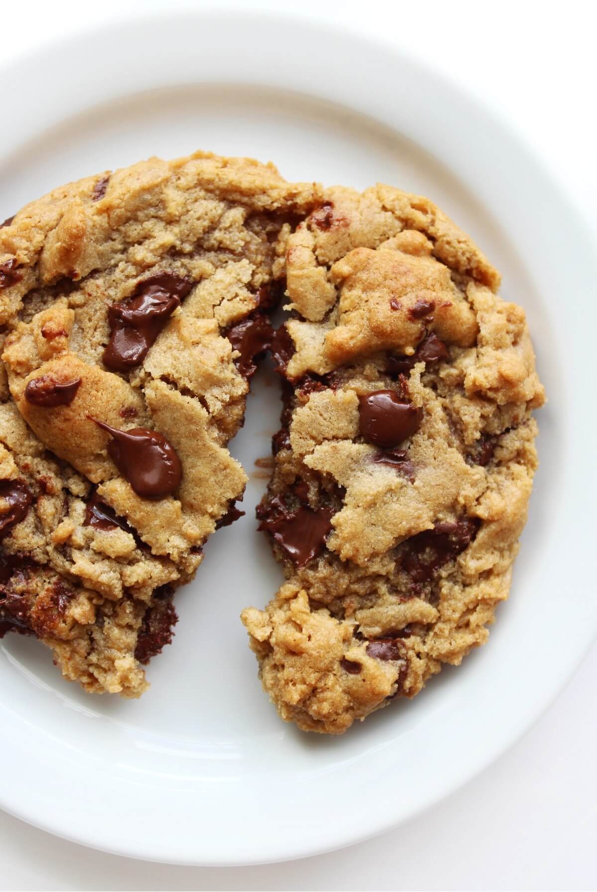 close up of large vegan chocolate chip cookies broken in half on white plate