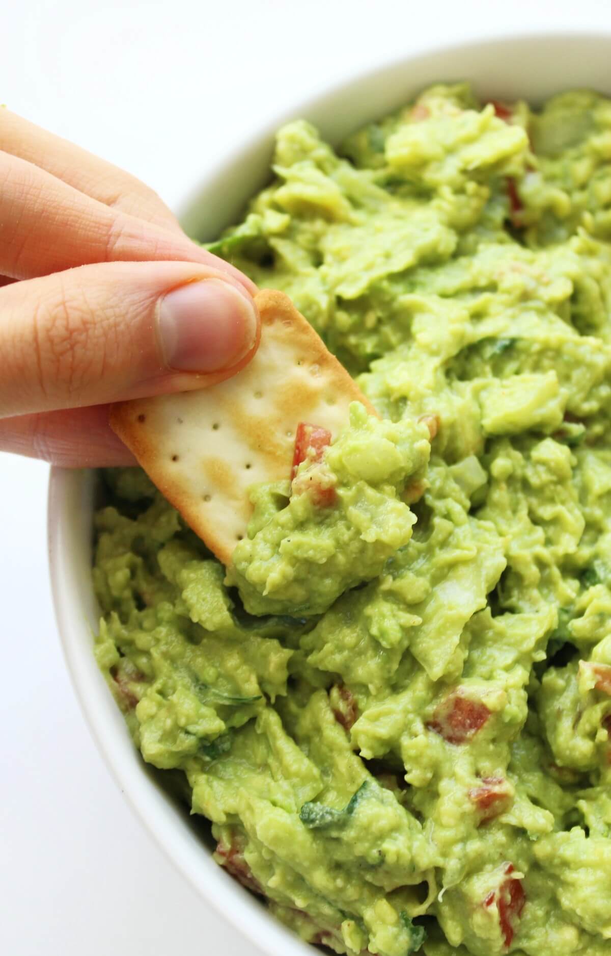 hand scooping guacamole with cracker