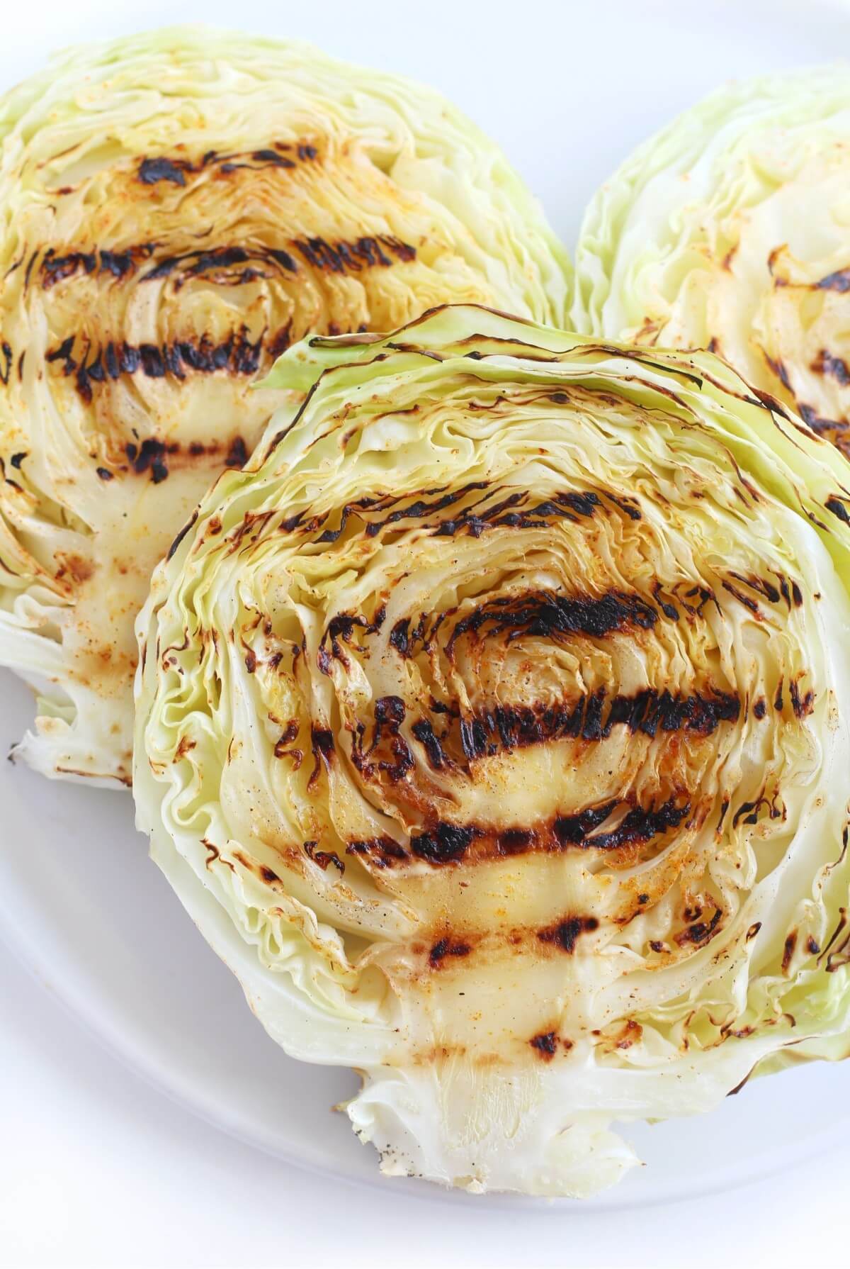 close up of three grilled cabbage steaks on white plate