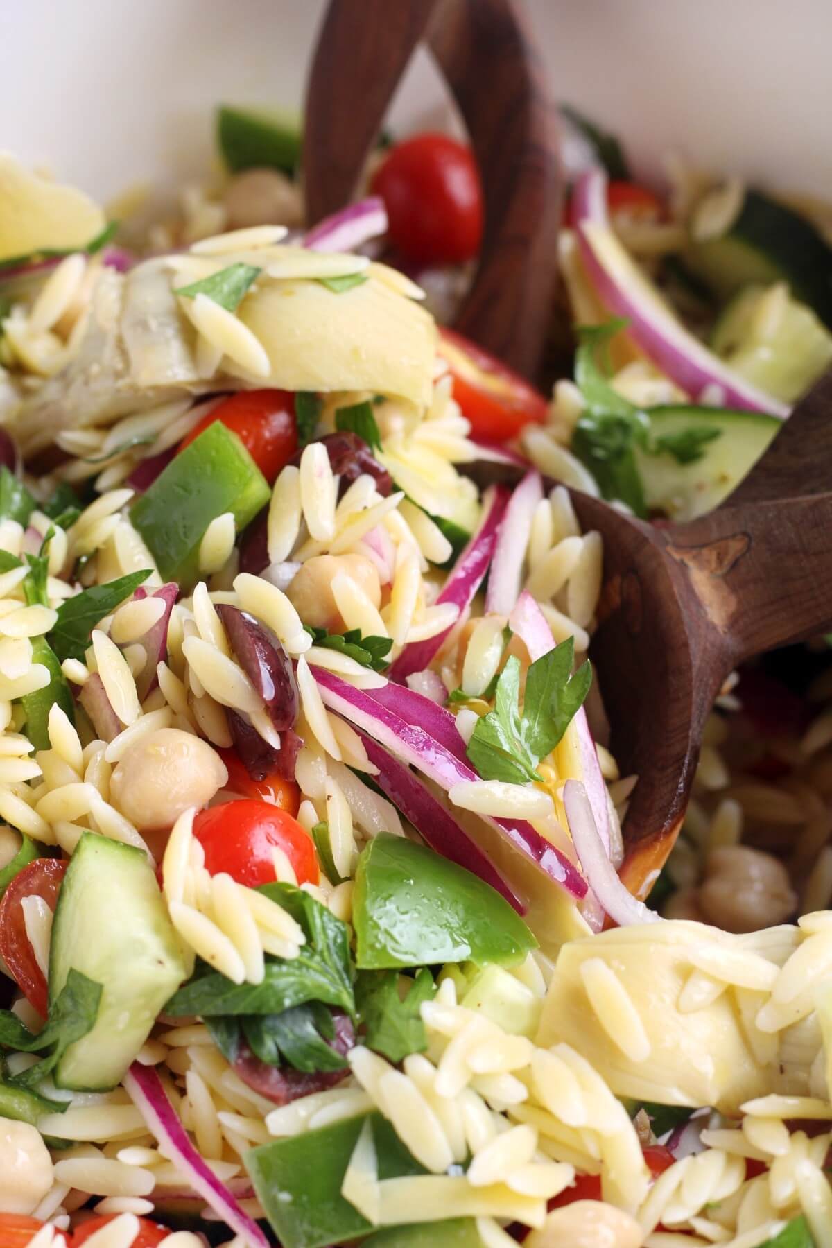 close up of gluten-free orzo pasta salad with wooden serving spoons