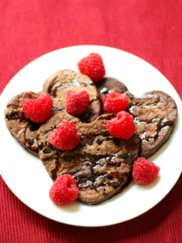 centered plate of finished valentine's day pancakes with chocolate syrup and raspberries