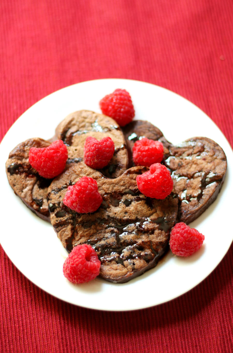 centered plate of finished valentine's day pancakes with chocolate syrup and raspberries