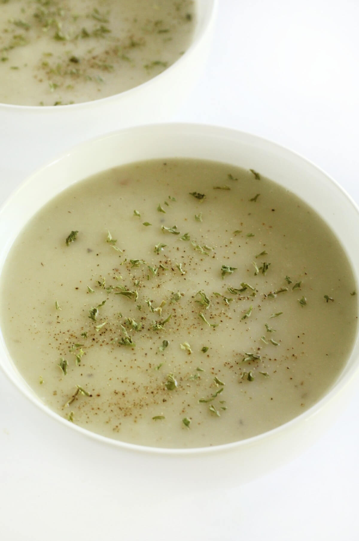 close up of bowl of vegan cream of malanga soup in white bowls