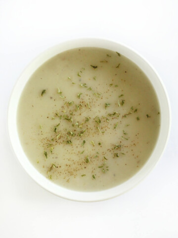 centered overhead view of vegan malanga soup in white bowl with black pepper and dried parsley