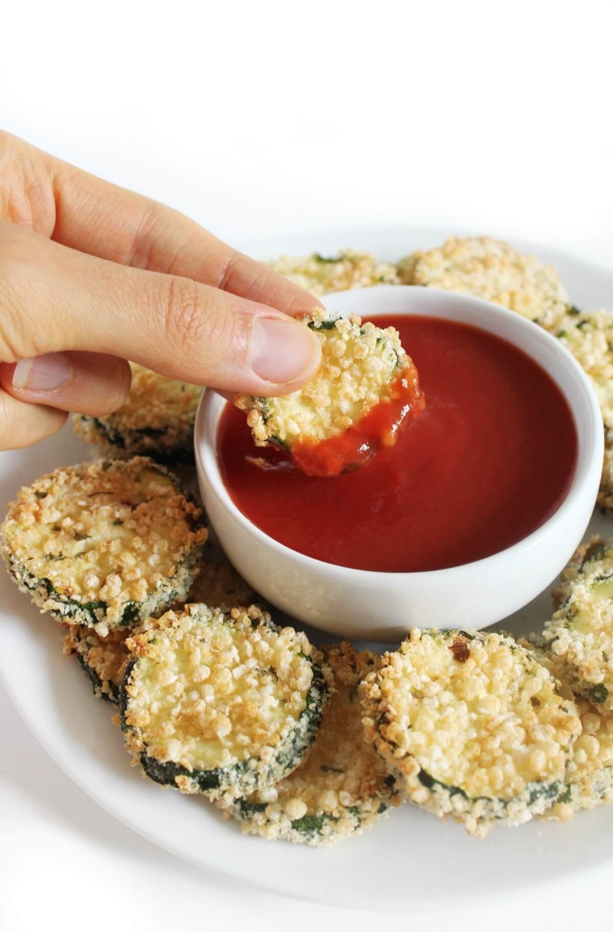 hand dipping air fryer zucchini chip in tomato sauce