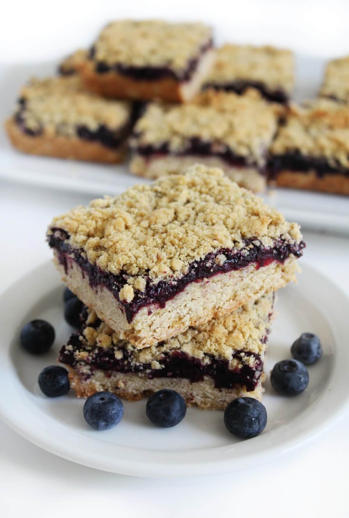 plate of gluten-free blueberry crumb bars with platter of bars in background