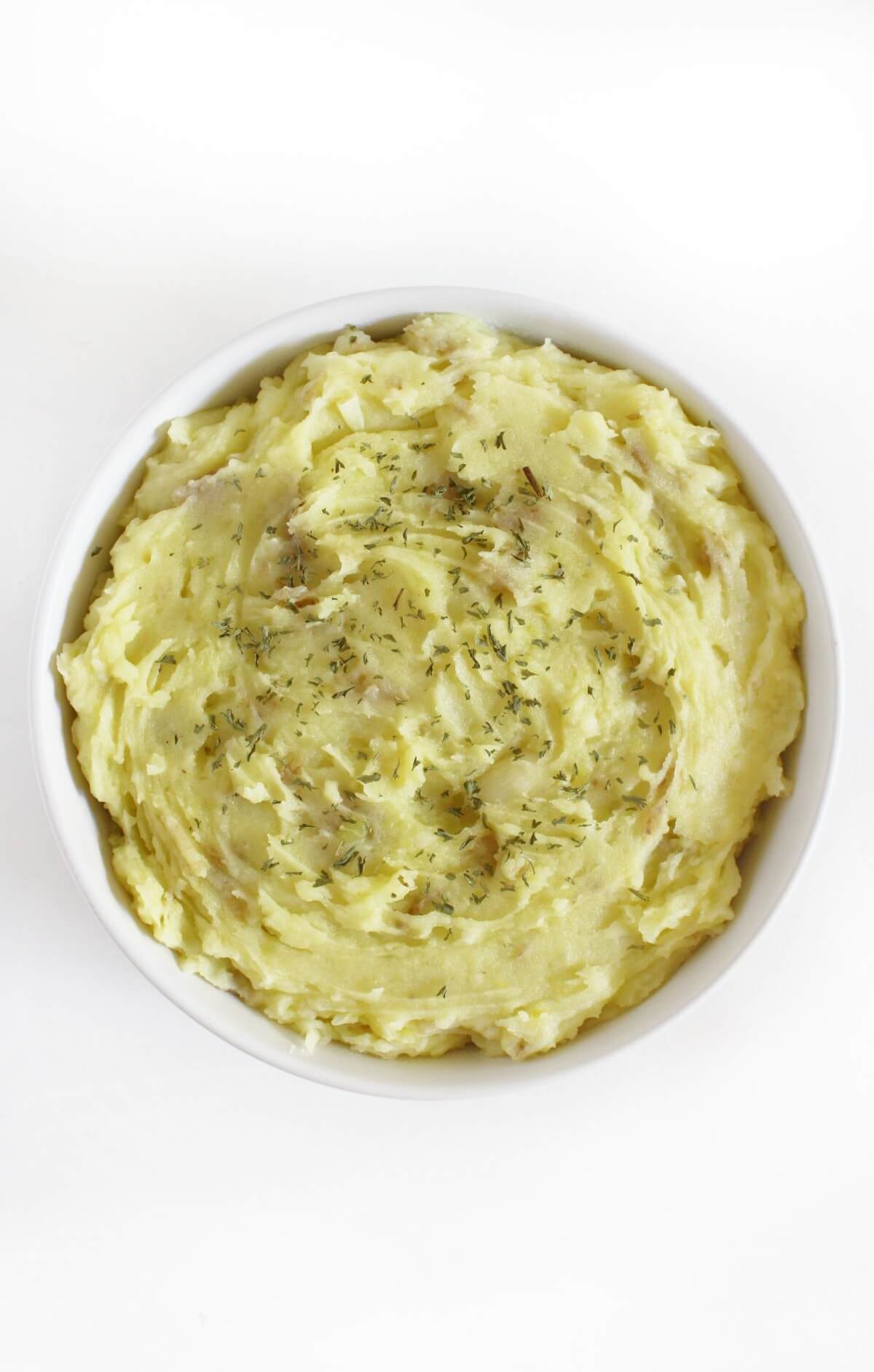 plain bowl of creamy vegan garlic mashed potatoes with dried thyme.