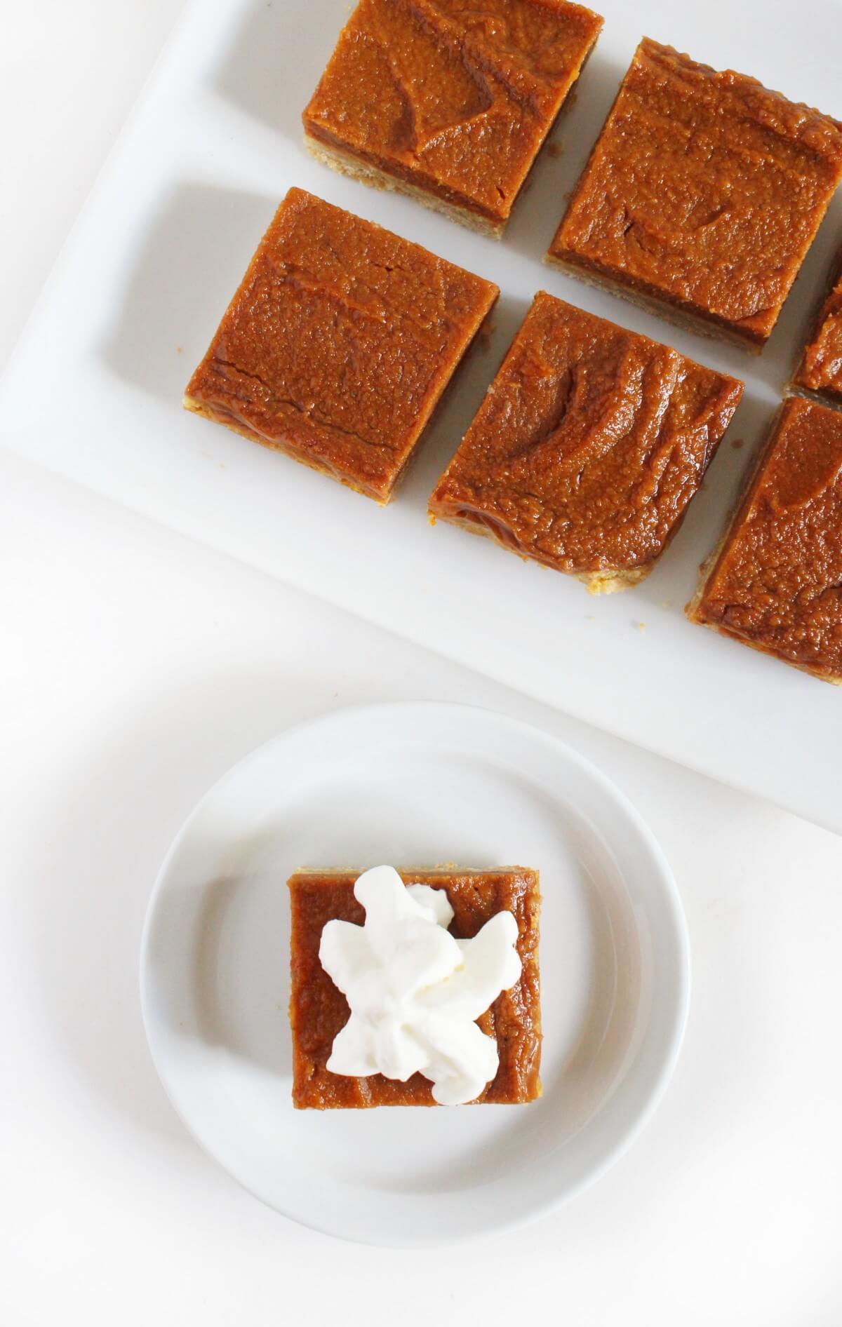 platter of gluten-free pumpkin pie bars with cut square served with vegan whipped cream on plate.