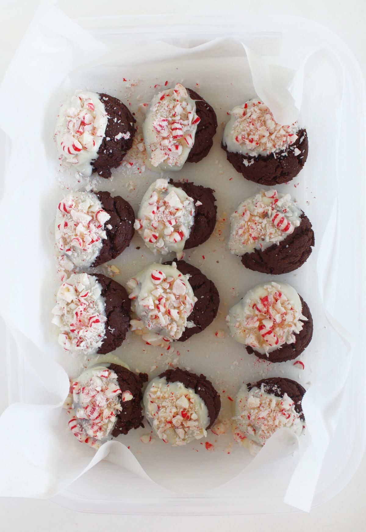dipping chocolate peppermint bark cookies in vegan white chocolate and crushed candy cane pieces.