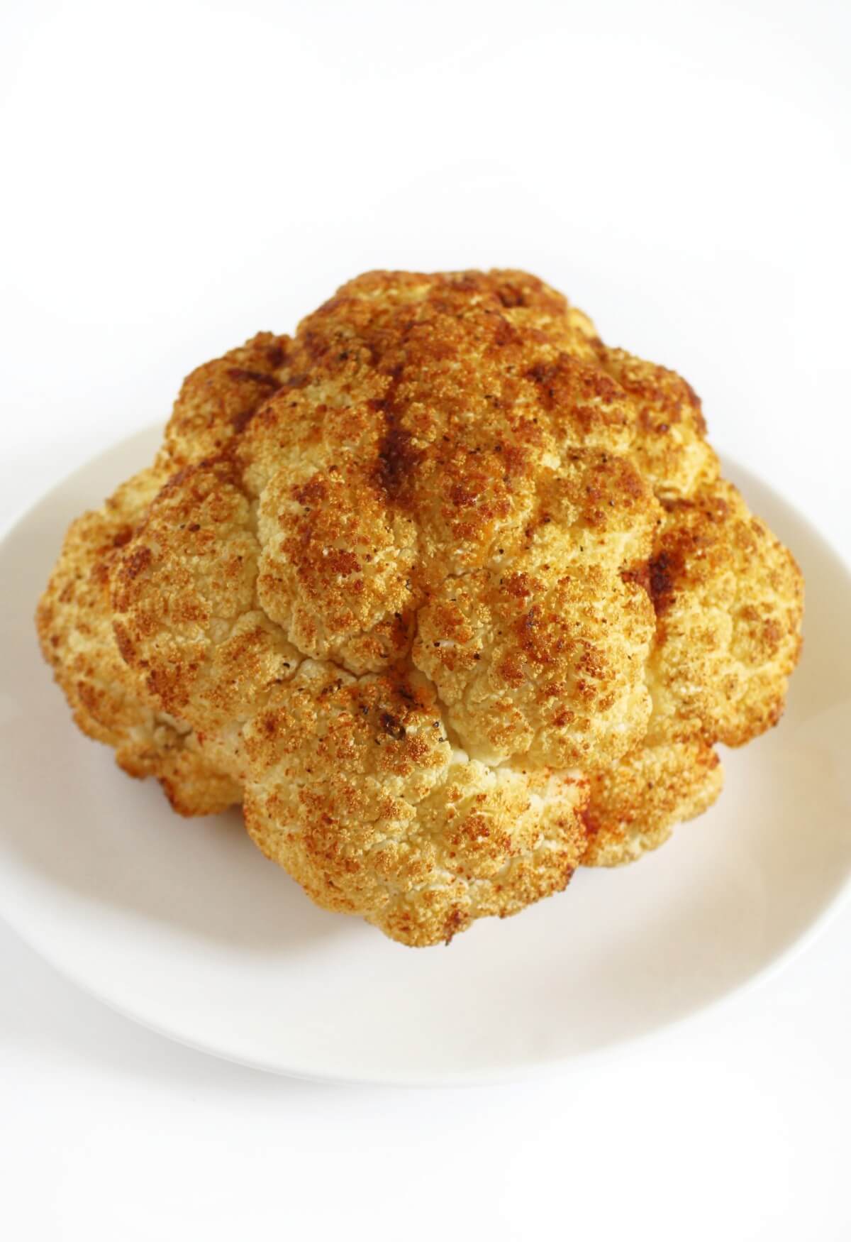 front of whole roasted cauliflower on white serving plate.