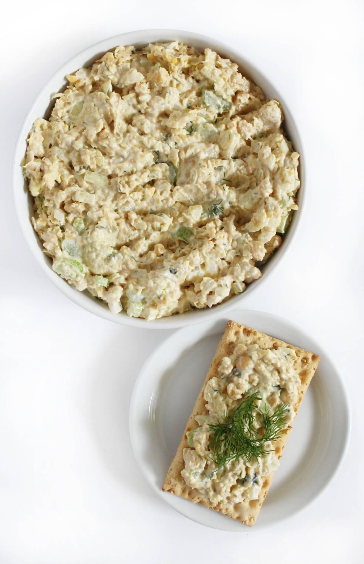 serving bowl of vegan tuna salad with single plate with cracker and chickpea tuna topping.