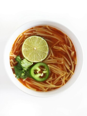single white bowl of vegan sopa de fideo with lime, jalapeno, cilantro.