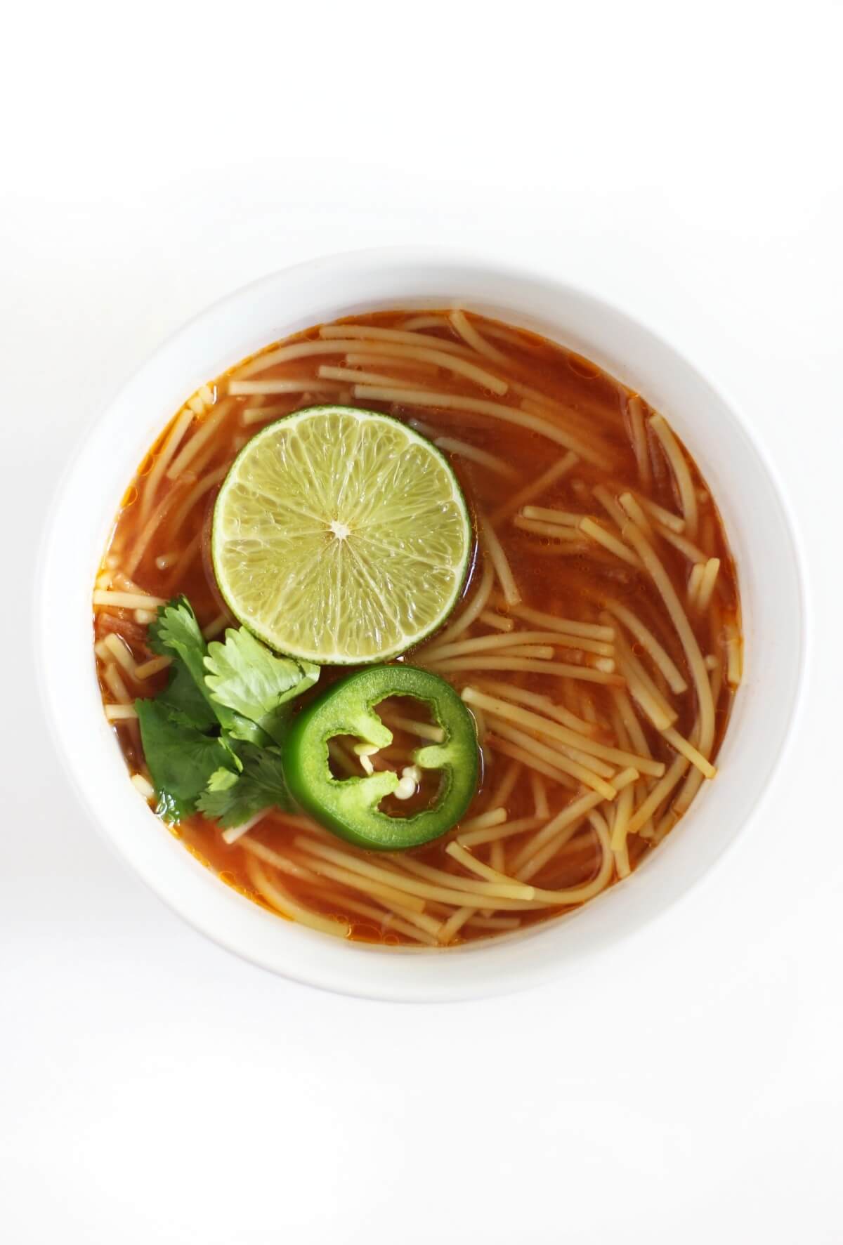 single white bowl of vegan sopa de fideo with lime, jalapeno, cilantro.