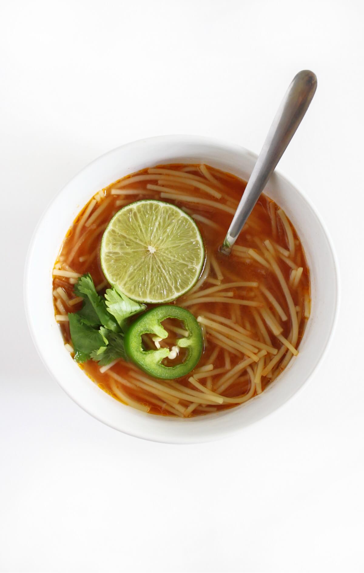 bowl of gluten-free sopa de fideo with metal spoon and toppings.