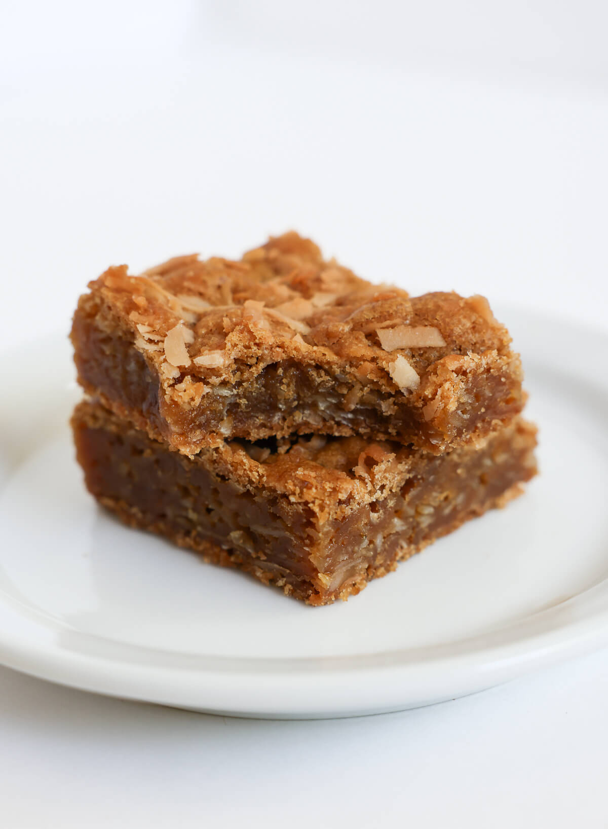 two stacked chewy coconut bars on plate.