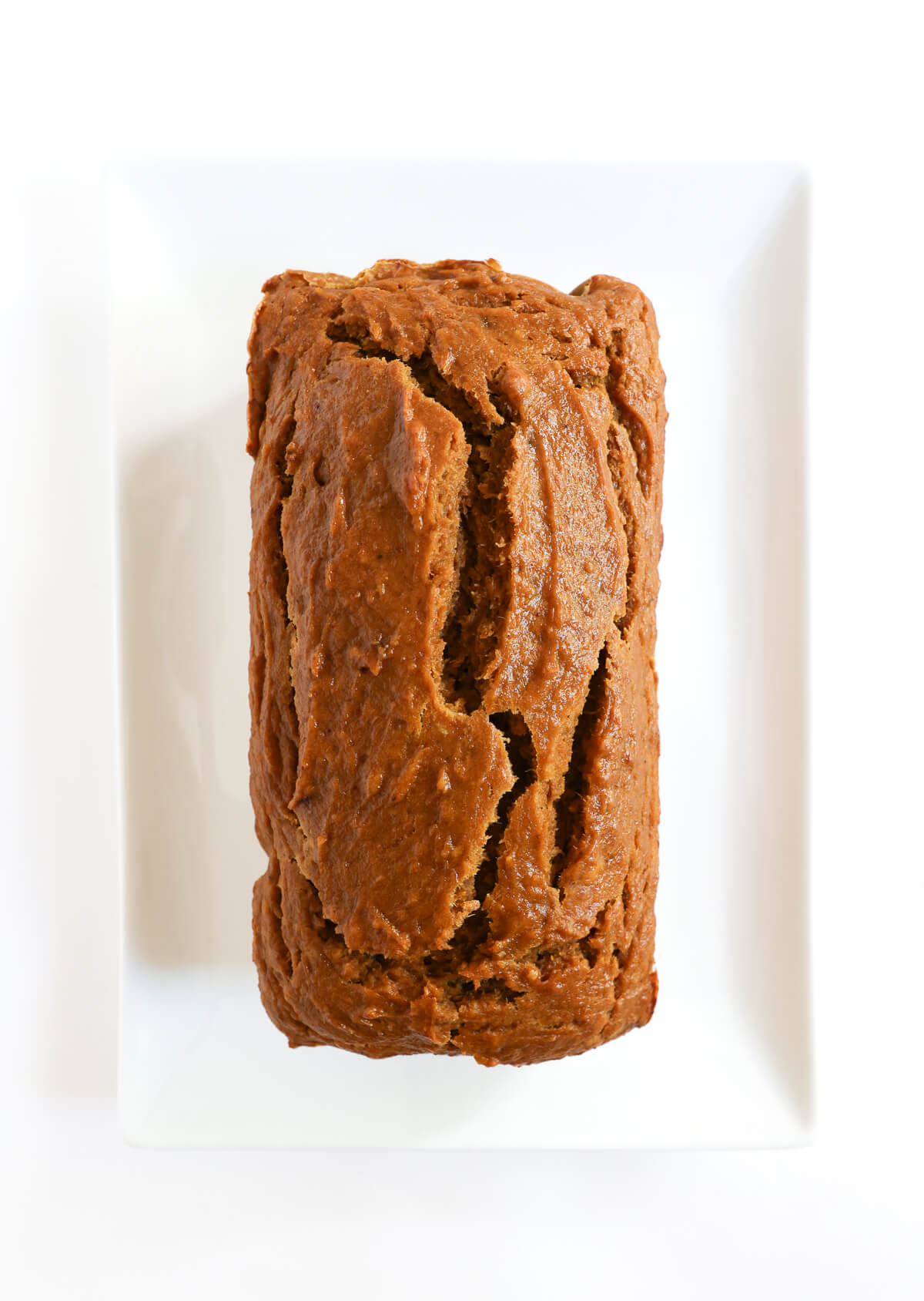 baked and unsliced loaf of pumpkin banana bread on plate.