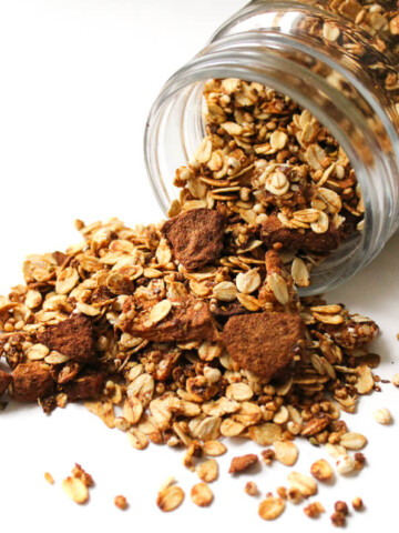 apple cinnamon granola spilled out of glass jar.