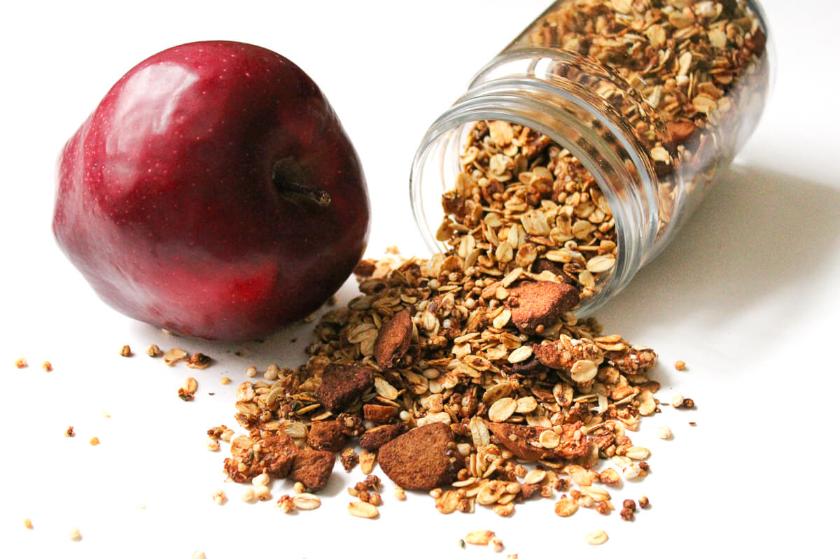 healthy apple cinnamon granola with whole apple sitting to side of jar.