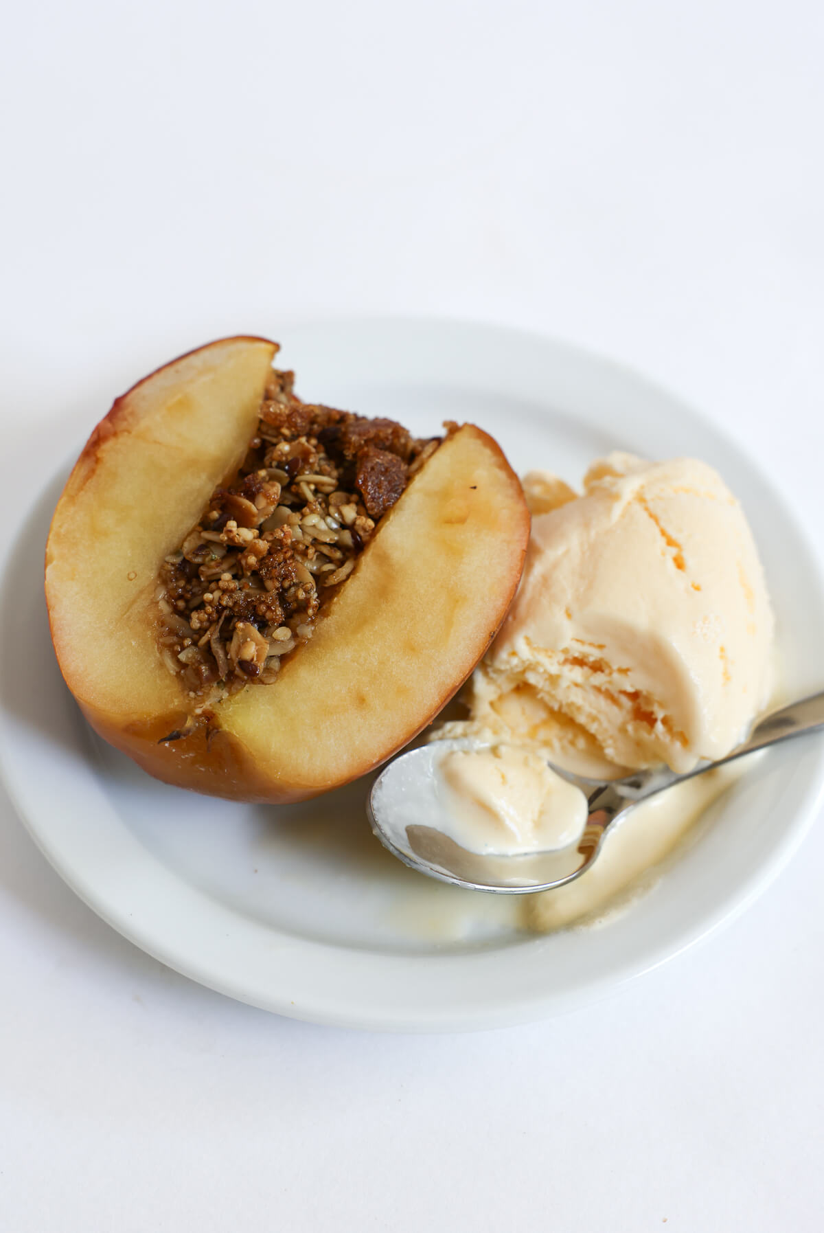 half a sliced open gluten-free baked apple with granola and ice cream on plate.