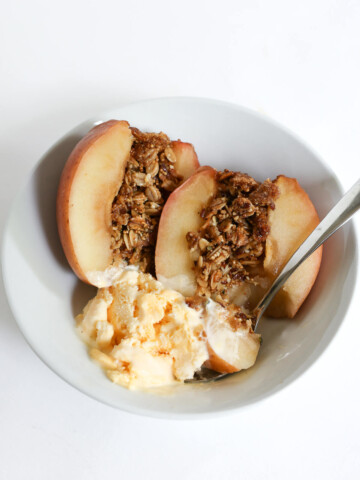 sliced open granola stuffed baked apple with ice cream in bowl.