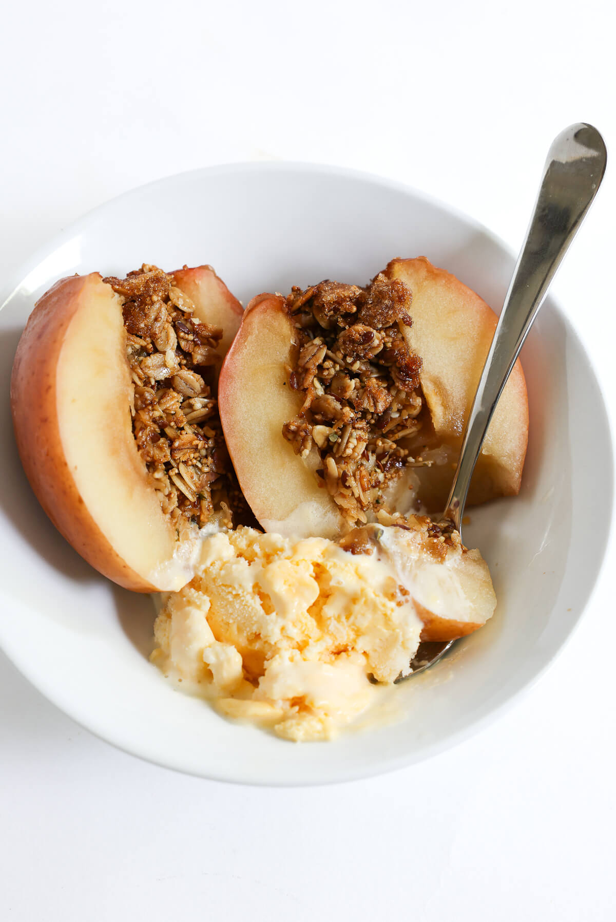 serving bowl with gluten-free baked apples stuffed with granola served with vegan ice cream.