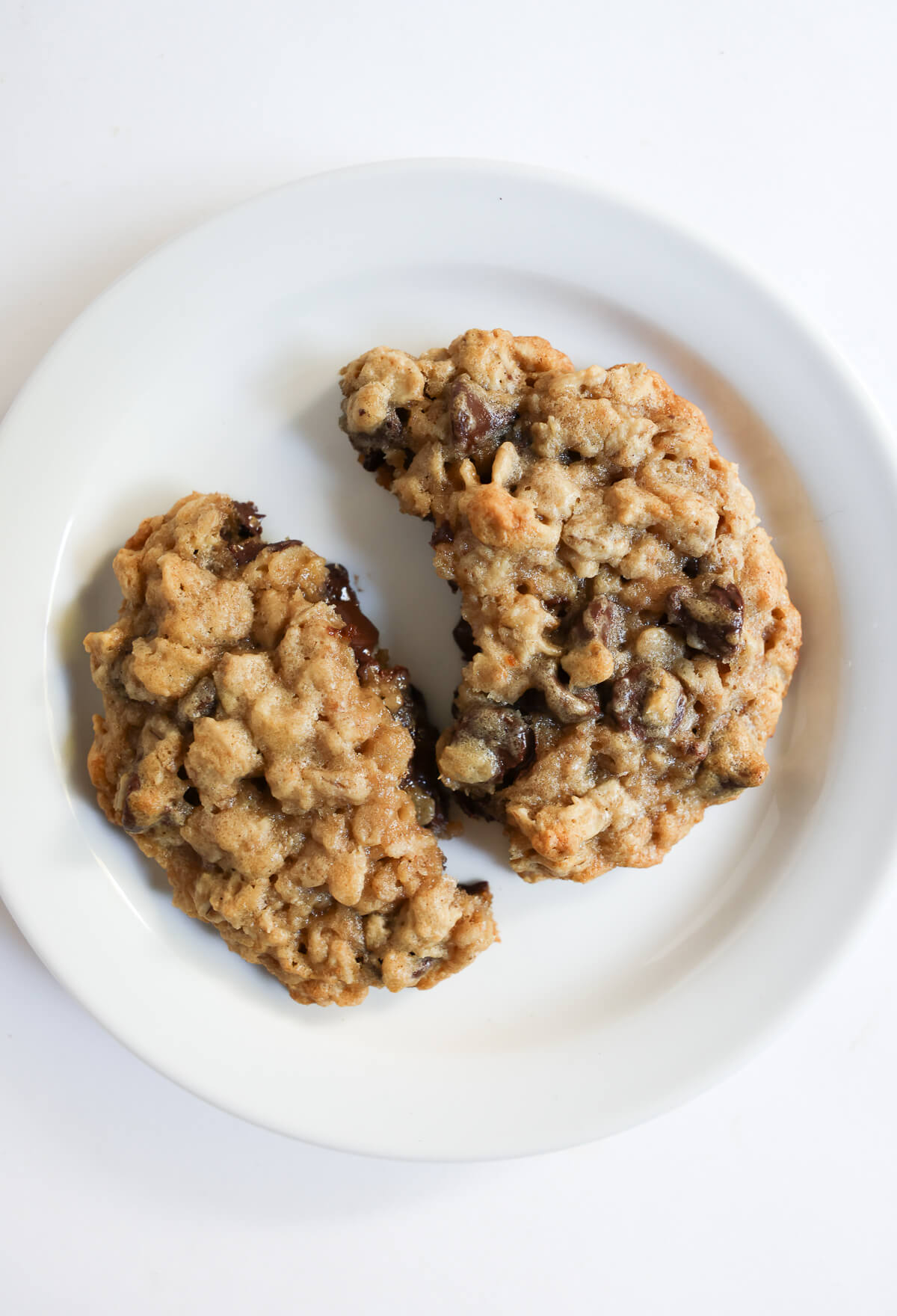 warm melty vegan oatmeal chocolate chip cookie broken in half on plate.