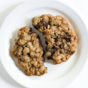 one large gluten-free oatmeal chocolate chip cookie on plate broken in half.