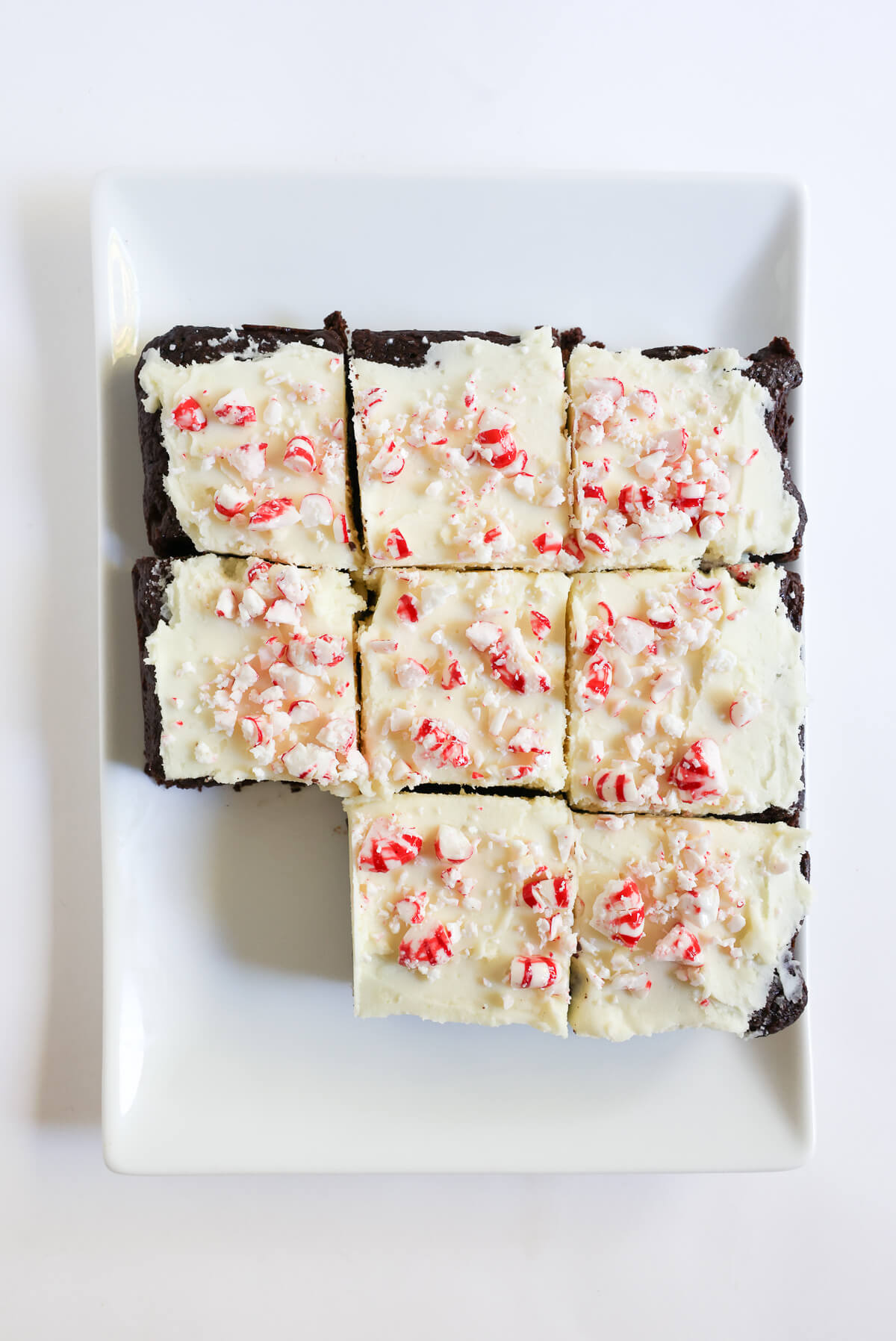 serving plate with sliced and frosted vegan peppermint bark brownies.