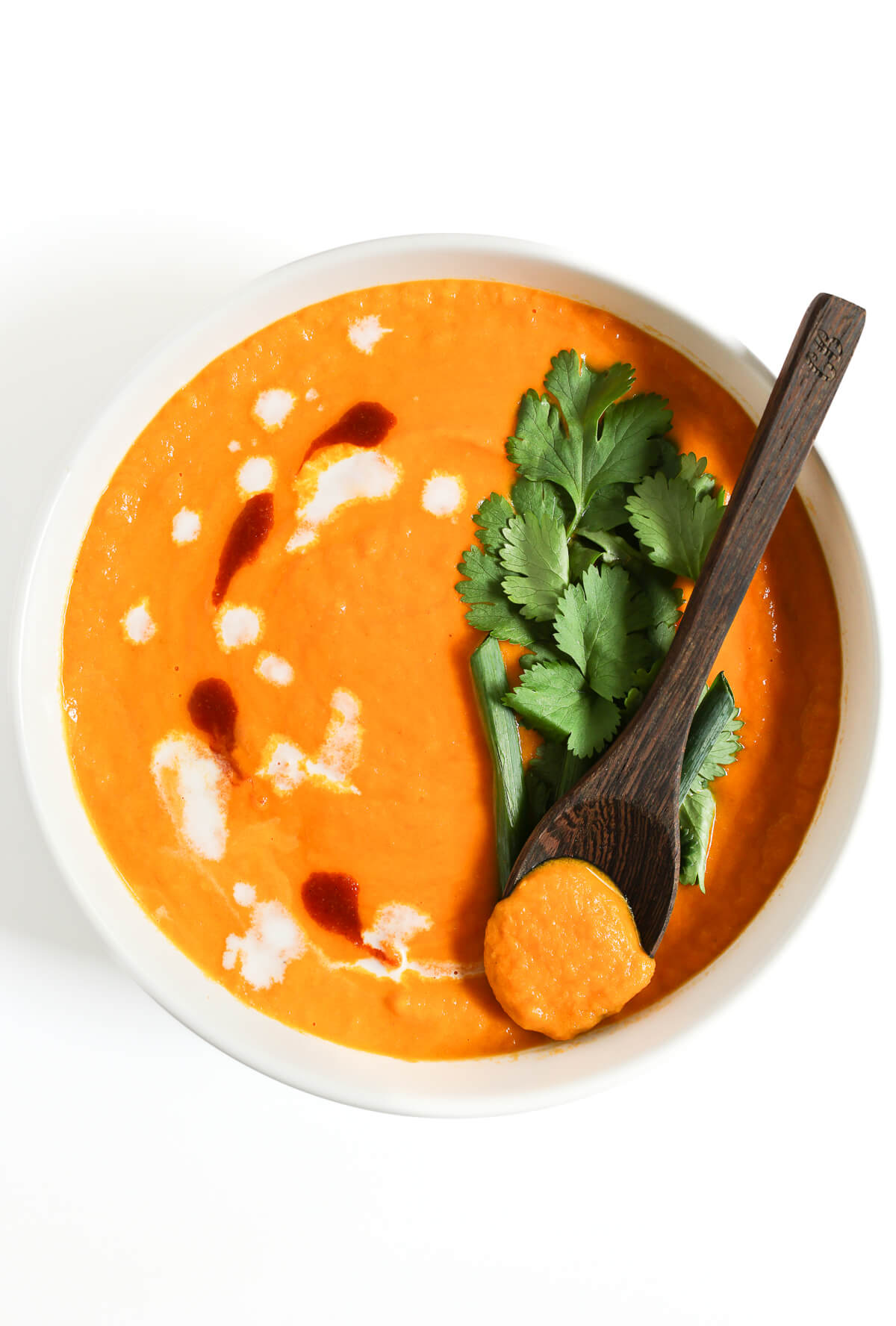 bowl of vegan thai carrot soup with wooden spoon scoop.